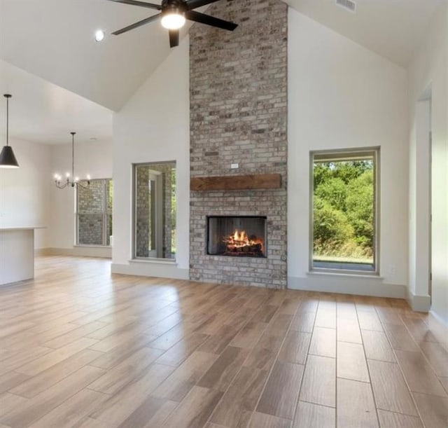 unfurnished living room featuring a brick fireplace, ceiling fan with notable chandelier, and high vaulted ceiling