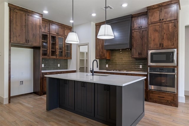 kitchen with decorative backsplash, sink, hanging light fixtures, a kitchen island with sink, and appliances with stainless steel finishes