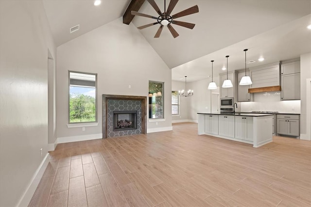 kitchen featuring ceiling fan with notable chandelier, an island with sink, hanging light fixtures, gray cabinets, and stainless steel microwave