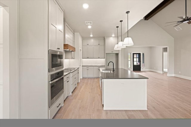 kitchen with stainless steel appliances, a kitchen island with sink, white cabinets, pendant lighting, and light hardwood / wood-style flooring