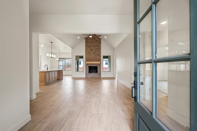 unfurnished living room featuring a large fireplace, light wood-style flooring, ceiling fan with notable chandelier, baseboards, and lofted ceiling