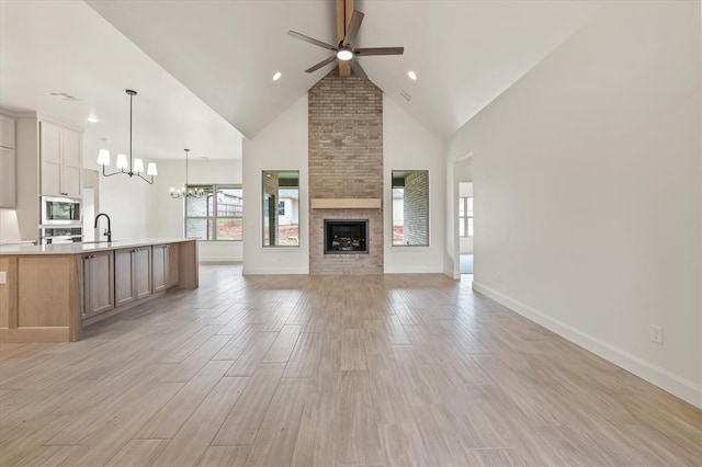 unfurnished living room featuring light wood-type flooring, a sink, high vaulted ceiling, baseboards, and ceiling fan with notable chandelier
