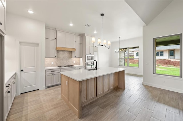 kitchen with gas cooktop, a sink, light countertops, stainless steel microwave, and backsplash