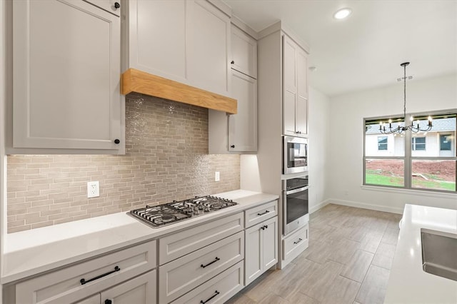 kitchen with backsplash, light countertops, baseboards, a notable chandelier, and stainless steel appliances