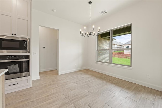 unfurnished dining area with visible vents, light wood-style floors, baseboards, and a chandelier
