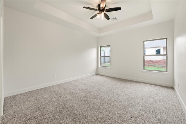 empty room featuring visible vents, a raised ceiling, baseboards, and light colored carpet