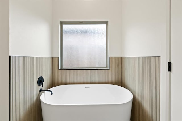 full bathroom featuring wainscoting, a healthy amount of sunlight, and a soaking tub