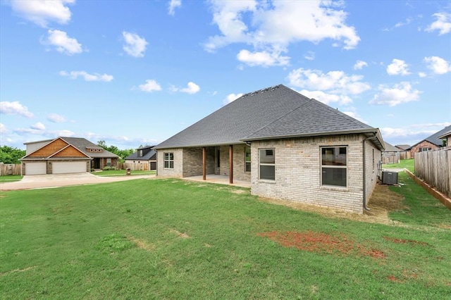 back of house featuring fence, a shingled roof, central AC, brick siding, and a lawn