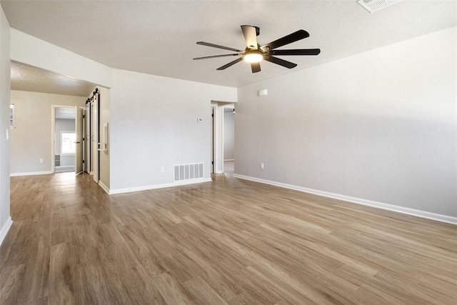 empty room with ceiling fan, wood finished floors, visible vents, and baseboards