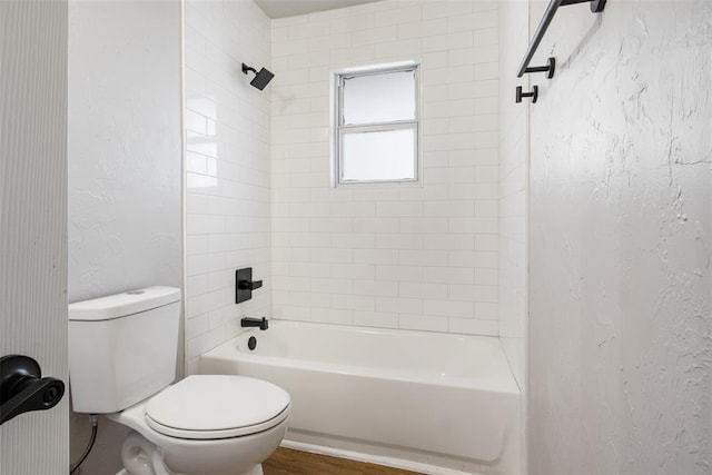 bathroom with wood finished floors, washtub / shower combination, toilet, and a textured wall