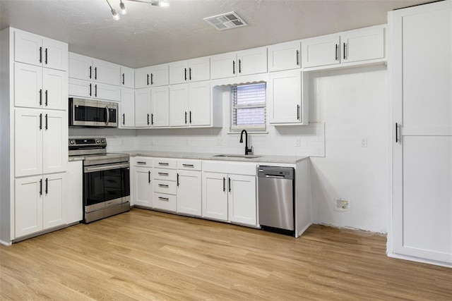 kitchen with a sink, stainless steel appliances, light wood-style floors, and visible vents