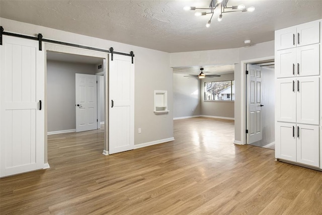 spare room with a barn door, baseboards, light wood-type flooring, and a textured ceiling