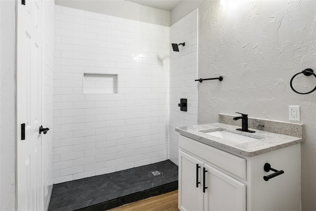 full bathroom featuring a tile shower, wood finished floors, vanity, and a textured wall