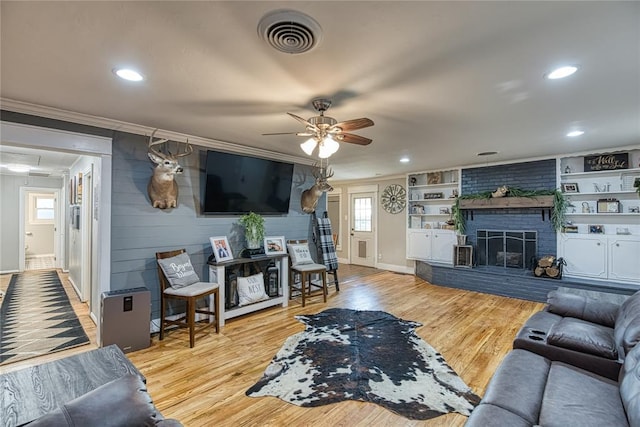 living room with hardwood / wood-style floors, a fireplace, built in features, ornamental molding, and ceiling fan