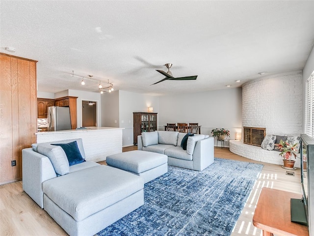 living room featuring ceiling fan, a brick fireplace, a textured ceiling, and light hardwood / wood-style floors