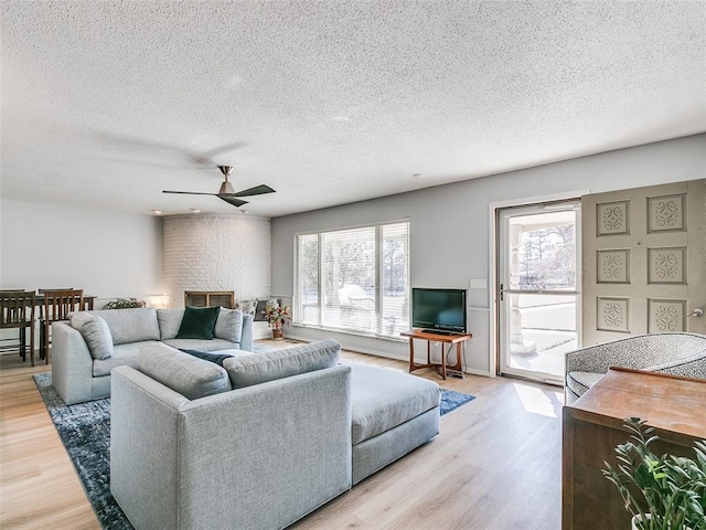 living room featuring hardwood / wood-style floors, a fireplace, a textured ceiling, and ceiling fan