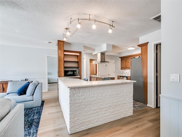 kitchen featuring island range hood, black appliances, a textured ceiling, and light wood-type flooring