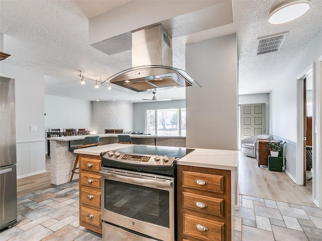 kitchen featuring track lighting, stainless steel appliances, a textured ceiling, and island exhaust hood