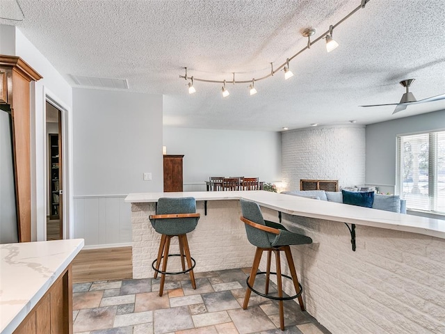 kitchen featuring a textured ceiling, stainless steel fridge, a breakfast bar, and ceiling fan