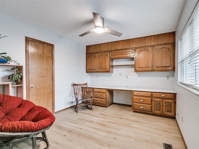 office space with ceiling fan, built in desk, a textured ceiling, and light hardwood / wood-style floors