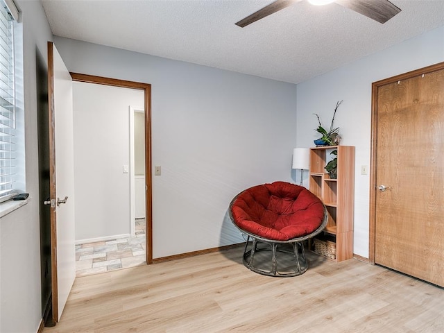 living area featuring ceiling fan, light hardwood / wood-style floors, and a textured ceiling