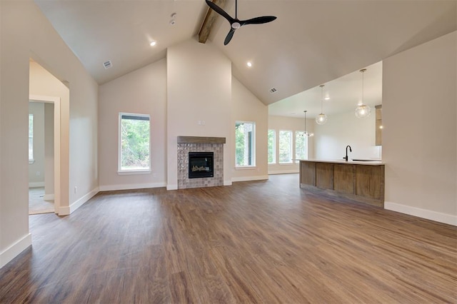 unfurnished living room with ceiling fan, beam ceiling, a fireplace, dark hardwood / wood-style floors, and high vaulted ceiling