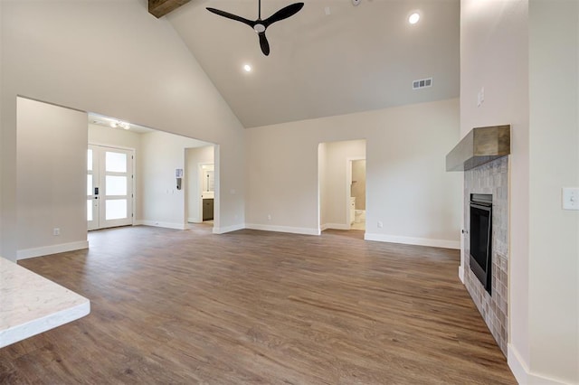 unfurnished living room with ceiling fan, a tiled fireplace, dark wood-type flooring, beam ceiling, and high vaulted ceiling