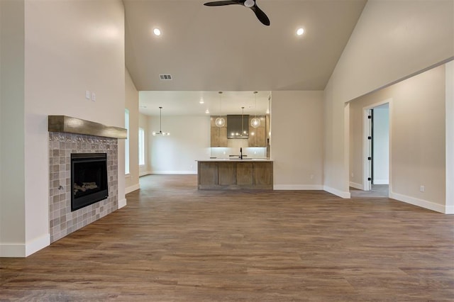 unfurnished living room with a towering ceiling, sink, dark hardwood / wood-style floors, ceiling fan, and a tile fireplace