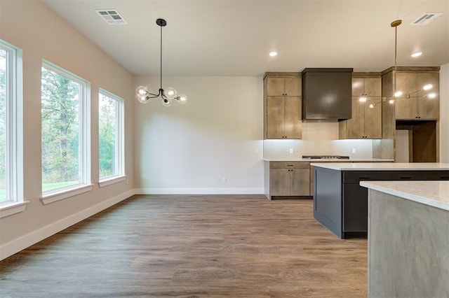kitchen featuring pendant lighting, tasteful backsplash, wall chimney range hood, light hardwood / wood-style floors, and an inviting chandelier