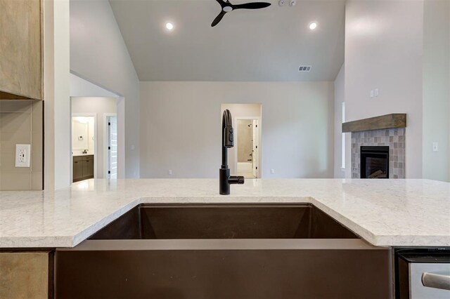 kitchen with light brown cabinetry, sink, a tiled fireplace, ceiling fan, and lofted ceiling