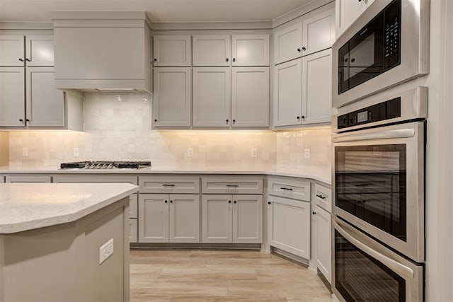 kitchen featuring custom range hood, decorative backsplash, stainless steel appliances, and light hardwood / wood-style floors