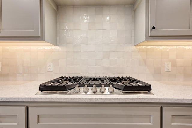 kitchen featuring tasteful backsplash, light stone countertops, stainless steel gas cooktop, and gray cabinetry