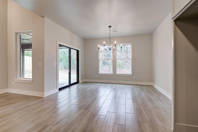 spare room featuring a chandelier and light wood-type flooring