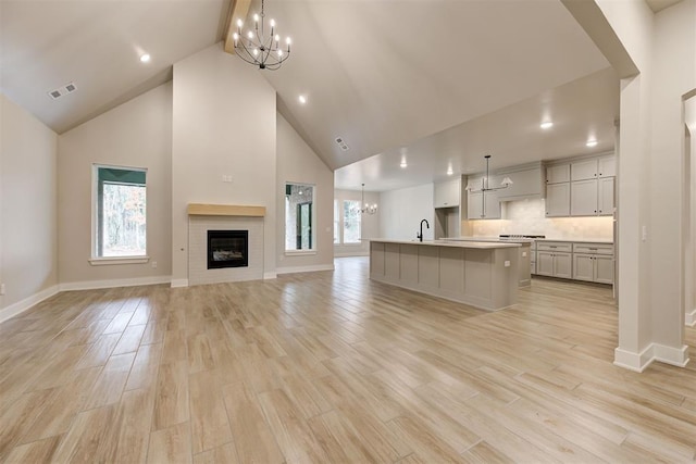 unfurnished living room featuring high vaulted ceiling, sink, a notable chandelier, and light wood-type flooring