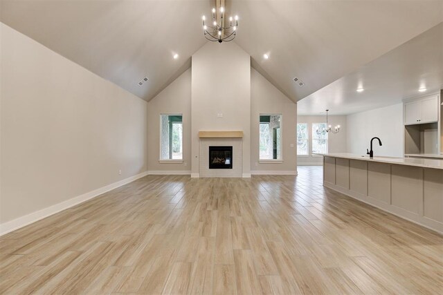 unfurnished living room with an inviting chandelier, high vaulted ceiling, and light wood-type flooring