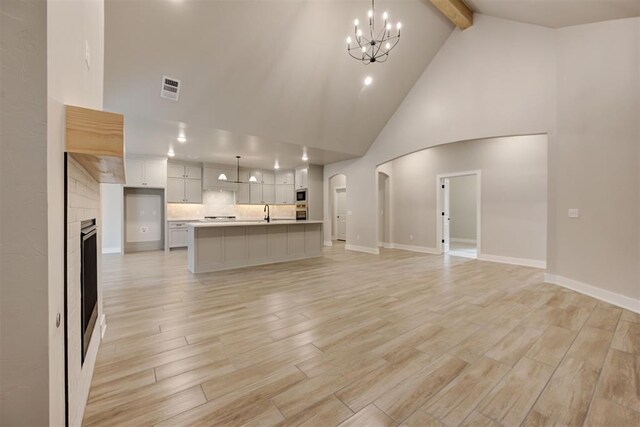 unfurnished living room with light hardwood / wood-style flooring, beam ceiling, high vaulted ceiling, a fireplace, and a chandelier