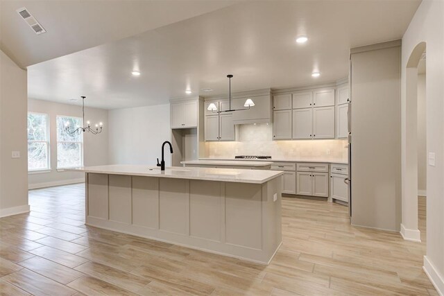 kitchen with pendant lighting, sink, tasteful backsplash, a center island with sink, and a chandelier