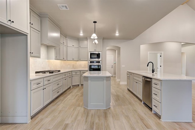 kitchen with light wood-type flooring, pendant lighting, stainless steel appliances, a kitchen island with sink, and decorative backsplash