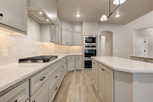 kitchen featuring a kitchen island, backsplash, custom exhaust hood, hanging light fixtures, and stainless steel appliances