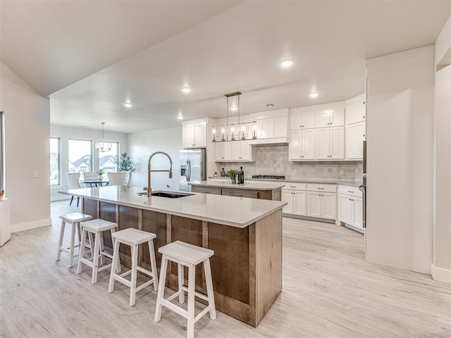 kitchen with tasteful backsplash, white cabinetry, hanging light fixtures, a kitchen island with sink, and a kitchen breakfast bar