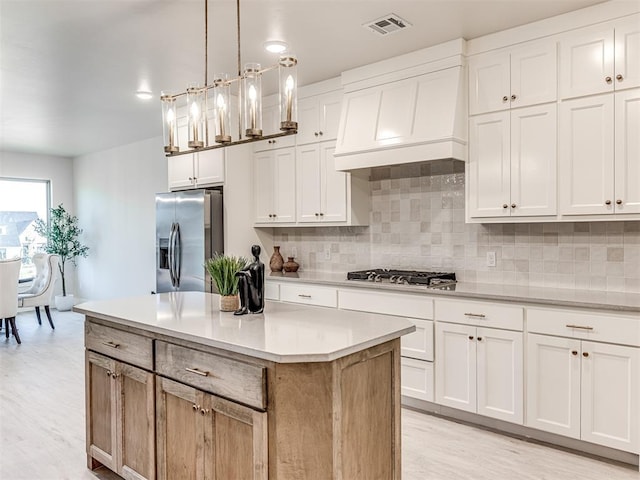 kitchen featuring white cabinets, appliances with stainless steel finishes, premium range hood, and pendant lighting