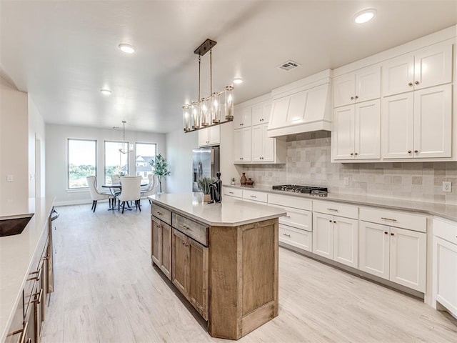 kitchen with pendant lighting, appliances with stainless steel finishes, premium range hood, white cabinets, and a center island