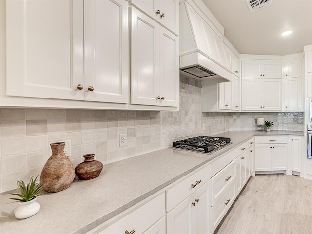 kitchen with white cabinets, appliances with stainless steel finishes, light hardwood / wood-style floors, premium range hood, and decorative backsplash