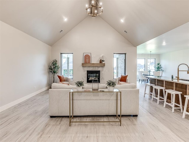 living room with light hardwood / wood-style floors, high vaulted ceiling, a notable chandelier, and a premium fireplace