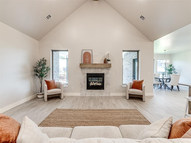 living room with light hardwood / wood-style floors, high vaulted ceiling, a high end fireplace, and an inviting chandelier