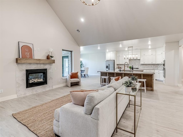 living room featuring sink, high vaulted ceiling, a chandelier, and a tiled fireplace