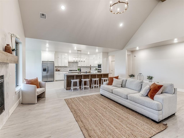 living room featuring a chandelier, high vaulted ceiling, a high end fireplace, and sink