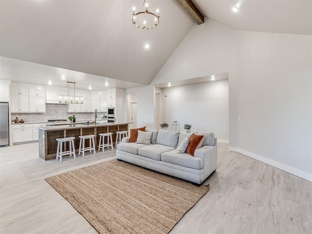 living room featuring sink, beam ceiling, high vaulted ceiling, light hardwood / wood-style floors, and a chandelier