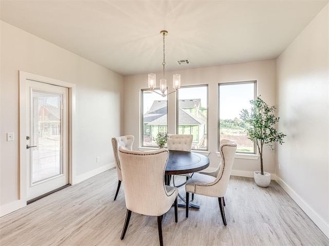 dining space with light wood-type flooring, a healthy amount of sunlight, and an inviting chandelier