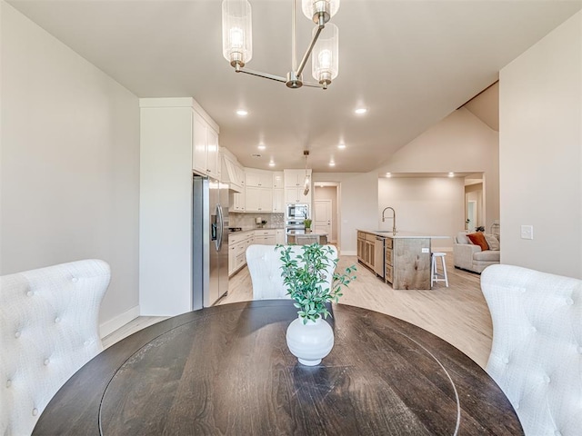 dining space with sink, a chandelier, light hardwood / wood-style flooring, and lofted ceiling